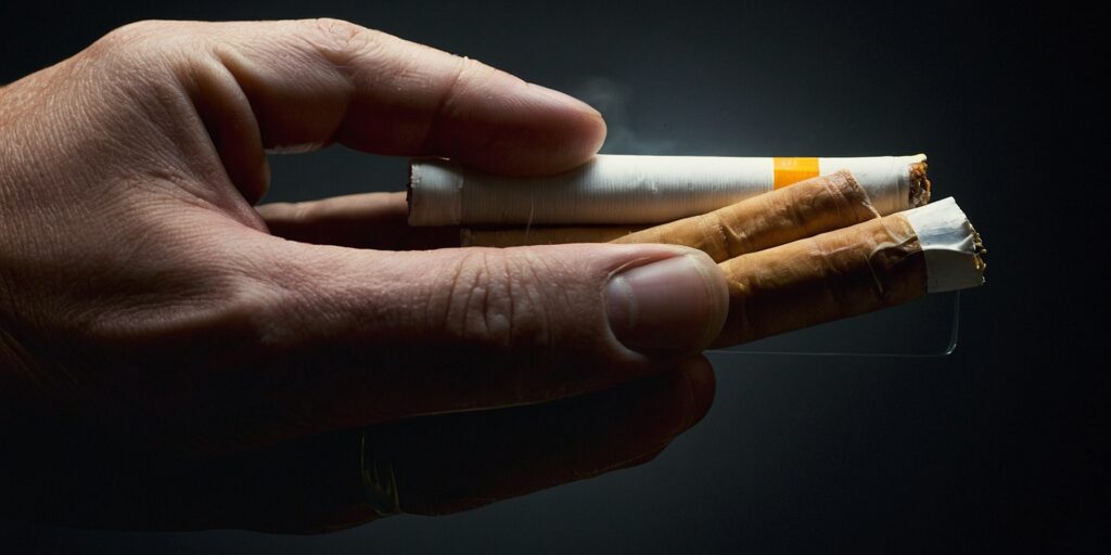 Image d'une personne tenant un patch à la nicotine dans une main et une cigarette dans l'autre, symbolisant le choix entre la cigarette et le sevrage.